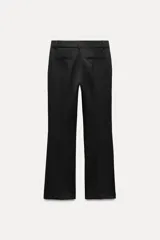 Pantalón negro de tiro medio con cintura con trabillas y corte flare. Cierre frontal con cremallera, botón y gancho metálico.