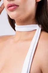Vestido corto blanco, ajustado al cuerpo, con efecto fruncido en el torso y falda con borde de tul transparente. Presenta un diseño strapless con una tira ancha que funciona como choker y se extiende como un tirante asimétrico.