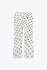 Pantalón largo de tiro alto con estampado de lunares negros sobre fondo blanco. Tiene falsos bolsillos de vivo en la espalda, detalle de solapa en el delantero y bajo acampanado. Se cierra con cremallera y gancho metálico.