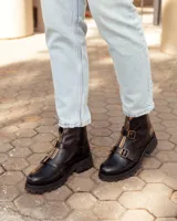 Botas de cuero negras con suela track, cierre frontal dorado y dos hebillas decorativas en el empeine.