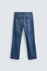 Pantalón de jean celeste de corte flare, con tiro medio, cinco bolsillos, cierre frontal con cremallera y botón, y bajo con acabado irregular.