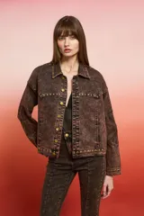 Campera de jean negra de corte holgado con detalles de tachas plateadas en costuras, hombros y puños, y bordado floral blanco en las mangas.