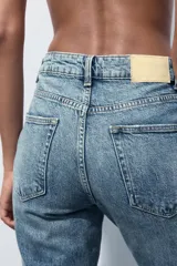 Pantalón de jean gris oscuro, de corte mom fit, tiro alto y largo tobillero. Cuenta con cinco bolsillos, cierre frontal con cremallera y botón.