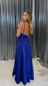 Vestido largo de fiesta color azul eléctrico con acabado brillante. Presenta un diseño con escote en V, tirantes finos y una falda con tajo lateral profundo.