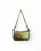 Cartera bandolera de cuero con correa regulable y cierre metálico frontal. Diseño compacto, práctico y moderno, con efecto iridiscente en tonos verdes, dorados y azules.
