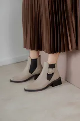 Botines Chelsea color beige con elásticos laterales negros, punta cuadrada, detalle de hebilla lateral y tacón bloque bajo.