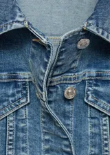 Chaqueta de jean azul de corte clásico con cuello de solapa, cierre frontal con botones metálicos, bolsillos delanteros con solapa y puños abotonados.