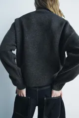 Jersey de punto color gris oscuro, de cuello alto y manga larga con terminaciones en rib.