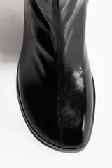 Botines negros de caña media, confeccionados en material con acabado charol brillante. Presentan punta cuadrada, caña ajustada tipo calcetín y un taco ancho y cuadrado.