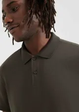 Polo verde oscuro de manga corta, confeccionada en algodón pima, con cuello clásico y tapeta de dos botones.