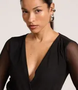 Body negro de tule con escote en V cruzado y mangas largas transparentes.