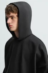 Sudadera con capucha negra, de corte oversize, confeccionada en tejido de algodón con interior en rizo. Cuenta con manga larga, bolsillos frontales tipo canguro, efecto lavado y acabados irregulares con vuelta.