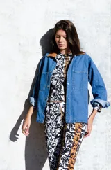 Campera de jean con cuello clásico, cierre frontal con botones metálicos, dos bolsillos de parche en el pecho y estampado floral en tonos verdes y marrones.