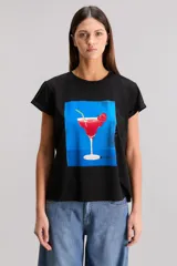 Remera negra de calce regular, confeccionada en jersey de algodón. Tiene cuello redondo, manga corta y estampado frontal de un trago con cereza sobre un fondo azul.