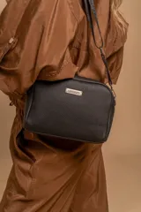 Bandolera compacta de color negro con textura granulada, correa ajustable negra con placa metálica que lleva el logo "LINCOLN'S".