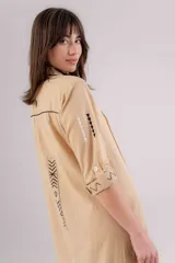 Vestido largo color crudo con bordados en negro, corte recto, cuello camisero y mangas 3/4 con puños abotonados.