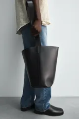 Bolso tipo shopper color marrón, fabricado en piel. Tiene un compartimento principal con cierre de imán y un bolsillo plano interior. El asa de hombro también es de piel.