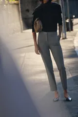 Pantalón gris de vestir, de corte tobillero, con tiro medio, cintura elástica en la parte trasera, bolsillos delanteros y falsos bolsillos traseros.