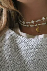 Collar doble de cuentas blancas con detalles dorados, dijes de perlas y dijes de estrellas. El collar inferior tiene un dije de luna dorada.