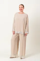 Blusa color beige con cuello redondo y mangas largas, con detalle de lentejuelas plateadas en el ruedo y los puños.