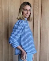 Blusa color beige con cuello con volados, mangas largas abullonadas con puños elásticos y cierre con botones en la parte delantera.