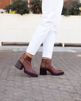 Botines de cuero marrón, hechos a mano en Uruguay, con plataforma delantera y taco ancho y alto de color negro. Presentan un detalle de textura de piel de reptil en la parte superior del talón y cierre lateral con cremallera.