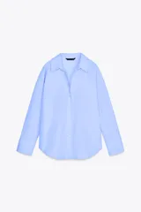 Camisa celeste de popelina de algodón, con cuello solapa, escote pico, manga larga con puños y cierre frontal con botones.