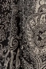 Camisa de viscosa con estampado paisley en blanco y negro. Cuello redondo con escote pico ajustable con cordones, mangas largas con elástico y volantes en los puños, bajo asimétrico y cierre frontal con botones forrados.