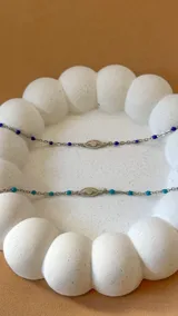 Pulsera de acero plateado con dije de ojo turco y cuentas de cristal azules.