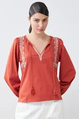 Remera blanca de estilo boho con bordados en el escote y mangas largas. Presenta escote en V con lazos y borlas. Corte recto y holgado.