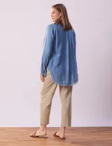 Camisa celeste de tencel marca Hester & Orchand, con cuello con solapa, escote en V y abertura central con botones. Tiene un bolsillo aplicado en la delantera y ruedo desflecado.