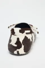 Zapato tipo mocasín en piel con pelo, con estampado animal, detalle de lazo en la parte delantera, pespunte en contraste y acabado en punta redonda.