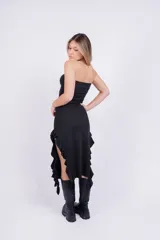 Vestido midi negro sin mangas, con escote strapless y volados asimétricos en el ruedo.