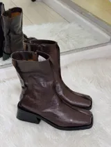 Botas cortas color chocolate con textura de cocodrilo, punta cuadrada y tacón bajo. Cuentan con cierre lateral.