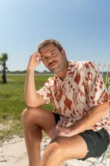 Camisa de manga corta con estampado abstracto en tonos naranja y blanco, cuello americano y botones de madera.