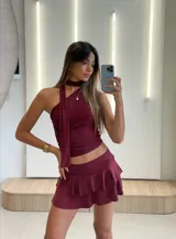 Conjunto de top halter y minifalda con volados color borgoña. El top es ajustado al cuerpo y tiene un lazo que se ata al cuello. La falda es de tiro bajo y tiene dos volados.