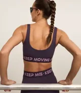 Top deportivo con breteles anchos, copas removibles, elástico estampado con la frase "Keep Moving" y espalda deportiva.