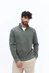 Buzo de algodón color verde musgo, con cuello alto y cierre frontal parcial. Presenta puños y cintura acanalados, y un pequeño logo bordado en el pecho.