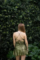 Vestido corto de lentejuelas color verde oliva, con escote en V, breteles finos cruzados en la espalda, cut-outs laterales y volado en el ruedo.