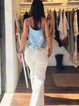 Musculosa celeste con breteles finos, escote en V y detalle de guarda calada con encaje en el ruedo. Tiene tres botones decorativos en el frente.