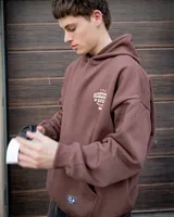 Canguro marrón con capucha, corte oversized y estampado frontal con texto en blanco.