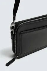 Bandolera negra con textura grabada, compartimento principal con cierre de cremallera, bolsillo interior con cremallera, bolsillo plano frontal, asa de hombro ajustable y extraíble.