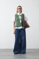 Chaleco tejido de punto color beige con trama texturada y diseño liviano. Presenta cuello a la base, silueta recta y cierre frontal mediante tres lazos delicados.