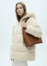 Campera puffer larga color beige, con capucha, cierre frontal con cremallera y bolsillos laterales con cierre.
