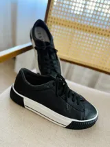 Zapatillas urbanas de cuero negro con cordones y plataforma blanca con suela negra.