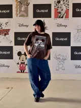 Remera marrón de manga corta y corte holgado, con estampado frontal de Mickey Mouse usando gafas de sol sobre un fondo de líneas onduladas y el texto "ALWAYS ON VACAY".