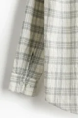 Camisa blanca con diseño a cuadros grises, de corte holgado, manga larga y cuello inglés.