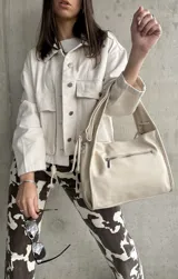 Sobrecamisa color crema con cuello camisero, cierre frontal con botones a presión, bolsillos de parche con solapa en el pecho y corte holgado.