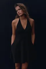 Vestido corto negro con cuello halter y lazada. Tiene bolsillos laterales ocultos y forro interior combinado. El cierre es en la espalda con cremallera oculta.