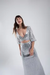 Vestido de fiesta de dos piezas plateado con lentejuelas. Top corto con mangas abullonadas y nudo en el frente. Falda larga ajustada.